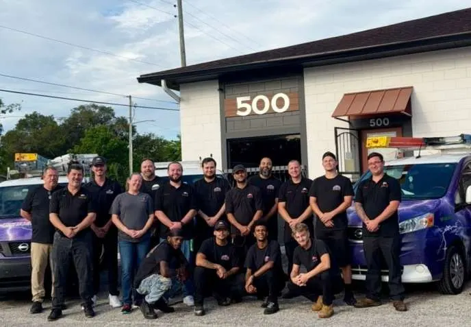 The In Phaze Electric crew lined up in front of the shop at 500 N Hudson Street in Orlando, between two purple company vans