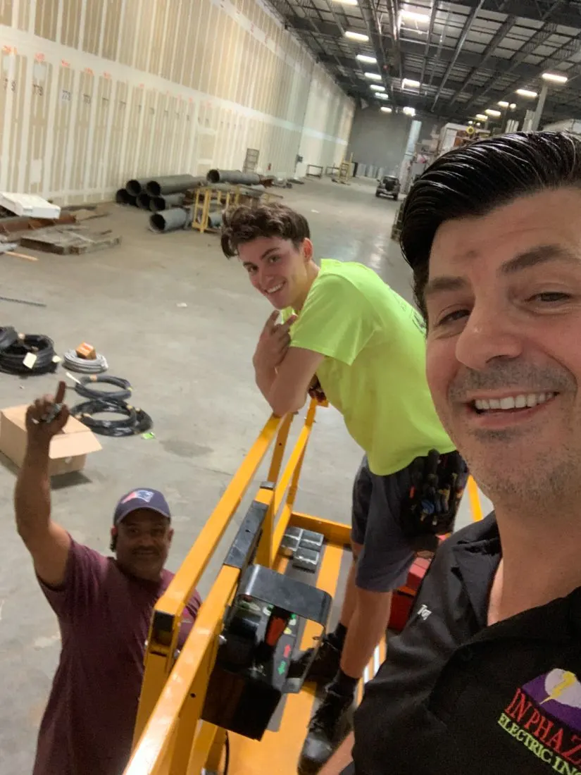 Tony Taylor, owner of In Phaze Electric, taking a selfie with two of his electricians on a scissor lift at a commercial job site